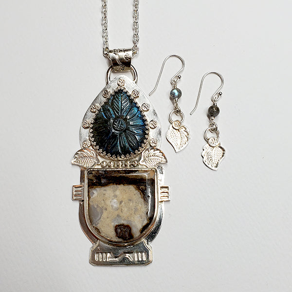 A handmade argentium silver pendant featuring a labradorite teardrop stone with raw mottled jasper stone set into the plant urn. This peacock blue Labradorite is full of sparkles and is hand carved. The tiny flower, leaf  and urn details on the setting are hand stamped and formed using of handmade stamps from the Navajo Nation.