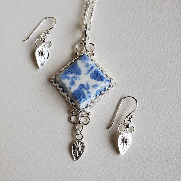 Sterling Silver Earring and Pendant set featuring  a One of a Kind Handmade porcelain  Diamond Shape focal cabochon. This wonderfully unique gift set features the use of the the art form of  Blue Transferware and was inspired by antique shipwrecked tableware shards. Set includes a  Complimentary 22 inch Sterling Silver Chain. The inverted tear drop shape embellishments are hand stamped using a handmade stamping tool from the Navajo Nation.