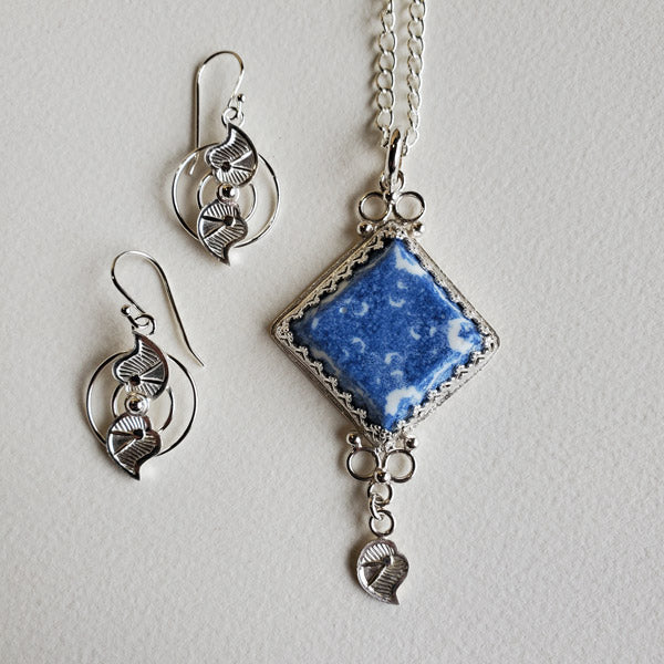 Sterling Silver Earring and Pendant set featuring  a One of a Kind Handmade porcelain  Diamond Shape focal cabochon. This wonderfully unique gift set features the use of the the art form of  Blue Transferware and was inspired by antique shipwrecked tableware shards. Set includes a  Complimentary 22 inch Sterling Silver Chain. The leaf shape embellishments are hand stamped and allude to the Yin and Yang symbol in the earrings to accompany the detail on the pendant.