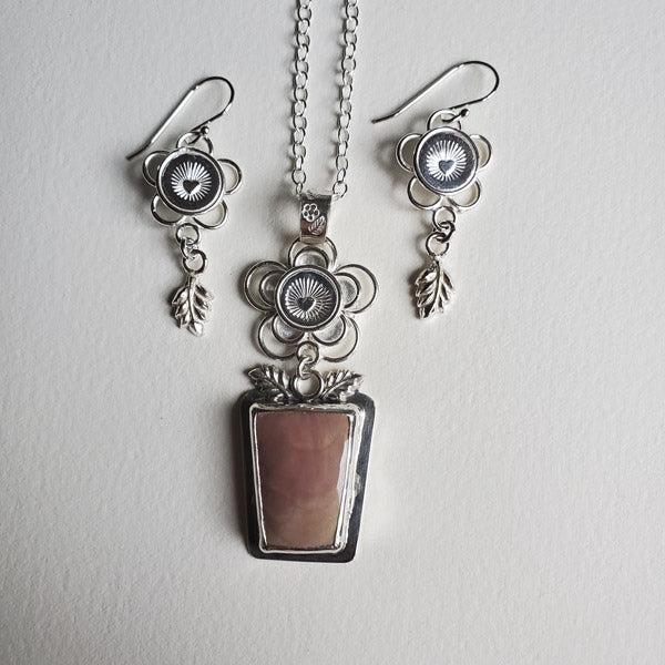 A one of a kind silver flower pot pendant set with a  lovely  dusty pink jasper stone and accompanying silver earrings. The flowers are 5 petal loops in the earrings and concentric stacked loops in the pendant with a radiant heart circular stamping in the center. The design is completed with a leaf dangle embellishment.